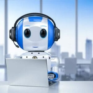 A small, blue and white robot wearing headphones sits at a desk with an open laptop in front of it, with a blurred office background.